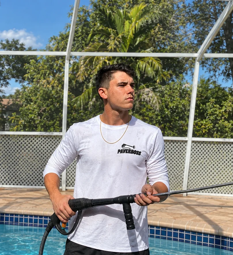 Tyler, owner of PaverBoss, holding a pressure-washing wand beside a pool